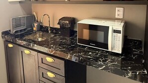 A kitchen with dark cabinets, a marble countertop, a microwave, and red pots on the shelf. - Beach Flat Sonne (João Pessoa)