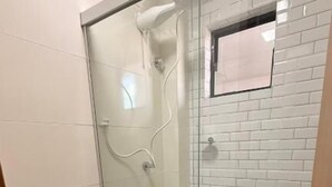 A bathroom with a glass-enclosed shower, a white toilet, and a tiled wall. - Beach Flat Sonne (João Pessoa)