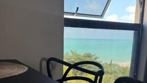 A table with a cup and saucer, a woven placemat, and a view of the ocean through a window. - Beach Flat Sonne (João Pessoa)