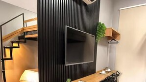 A modern kitchen with a built-in stove, a dining area with a wooden table and chairs, a black cabinet, and a mounted TV. - Beach Flat Sonne (João Pessoa)