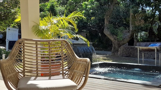 Uma cadeira de vime com almofada, mesa de vidro e piscina com cachoeira.