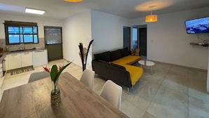 Um espaço de estar moderno com área de jantar, cozinha e televisão fixada na parede.