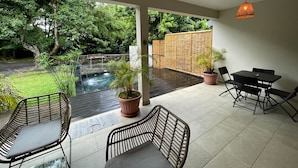 Um alpendre coberto com piscina, área de estar externa e vista para o jardim.
