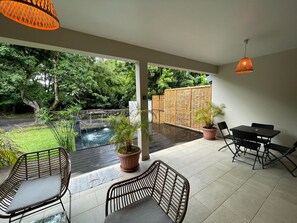 A covered patio with a pool, outdoor seating, and a view of the garden.