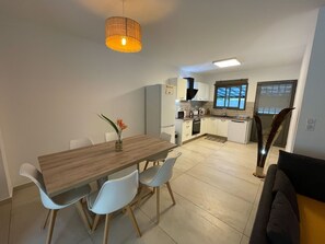 A compact kitchen with white cabinets, a wooden dining table, and a vase with flowers.