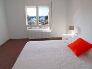 Ein Schlafzimmer mit Bett, Nachttisch, Lampe, einem Fenster mit Blick auf eine Marina und einer Heizung.