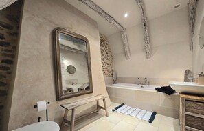 Un baño con bañera, lavabo, espejo, inodoro y un banco de madera.