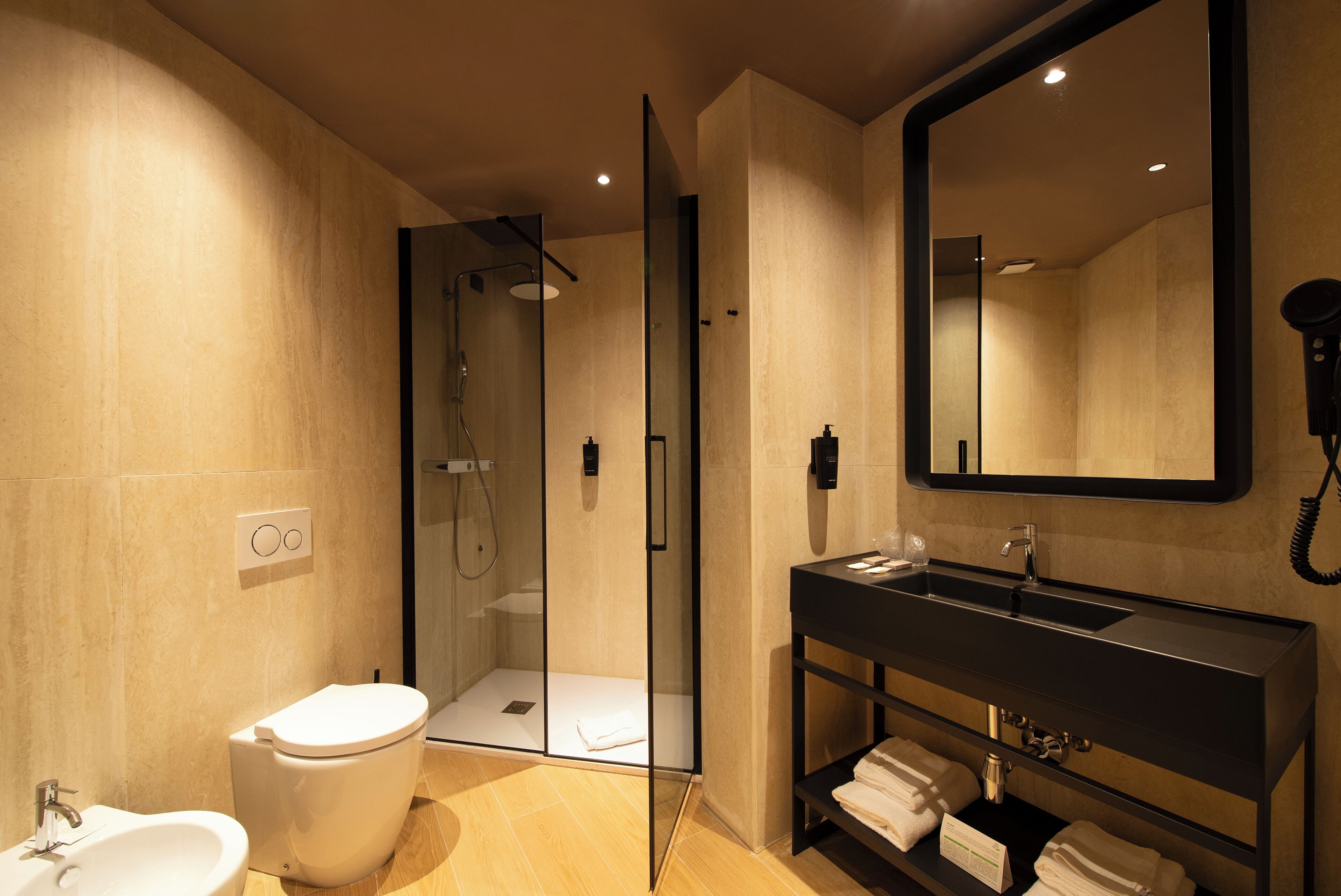 Une salle de bain moderne avec une douche à parois de verre, des toilettes blanches, un lavabo noir et un grand miroir.