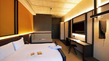 Una habitación de hotel con cama, escritorio, silla, televisor y armario.