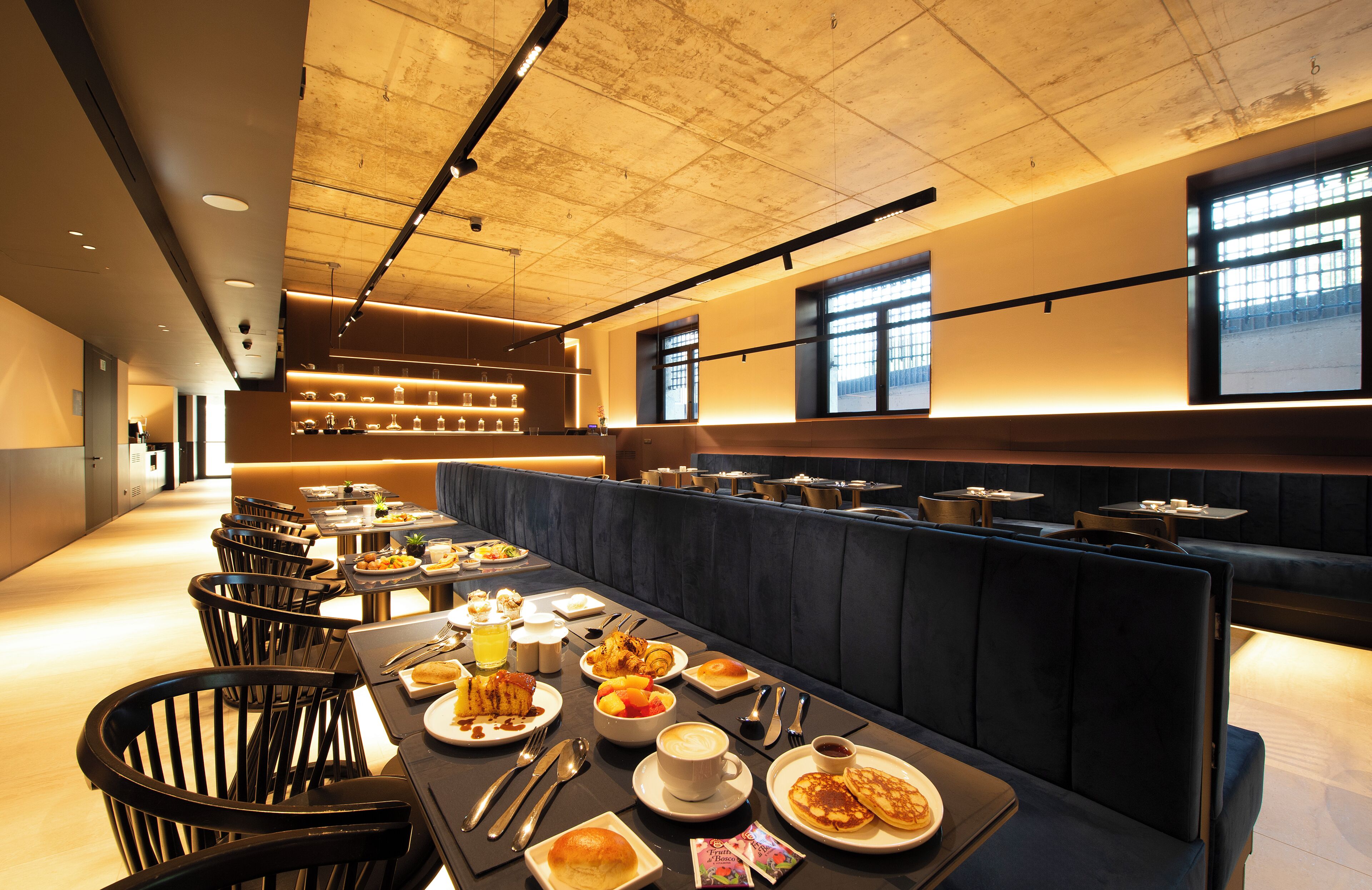 A restaurant with a long counter, multiple tables, and a high ceiling with exposed beams.