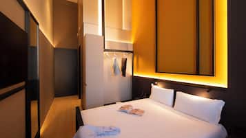 Una habitación de hotel con una cama, un armario, un espejo y una lámpara fijada a la pared.