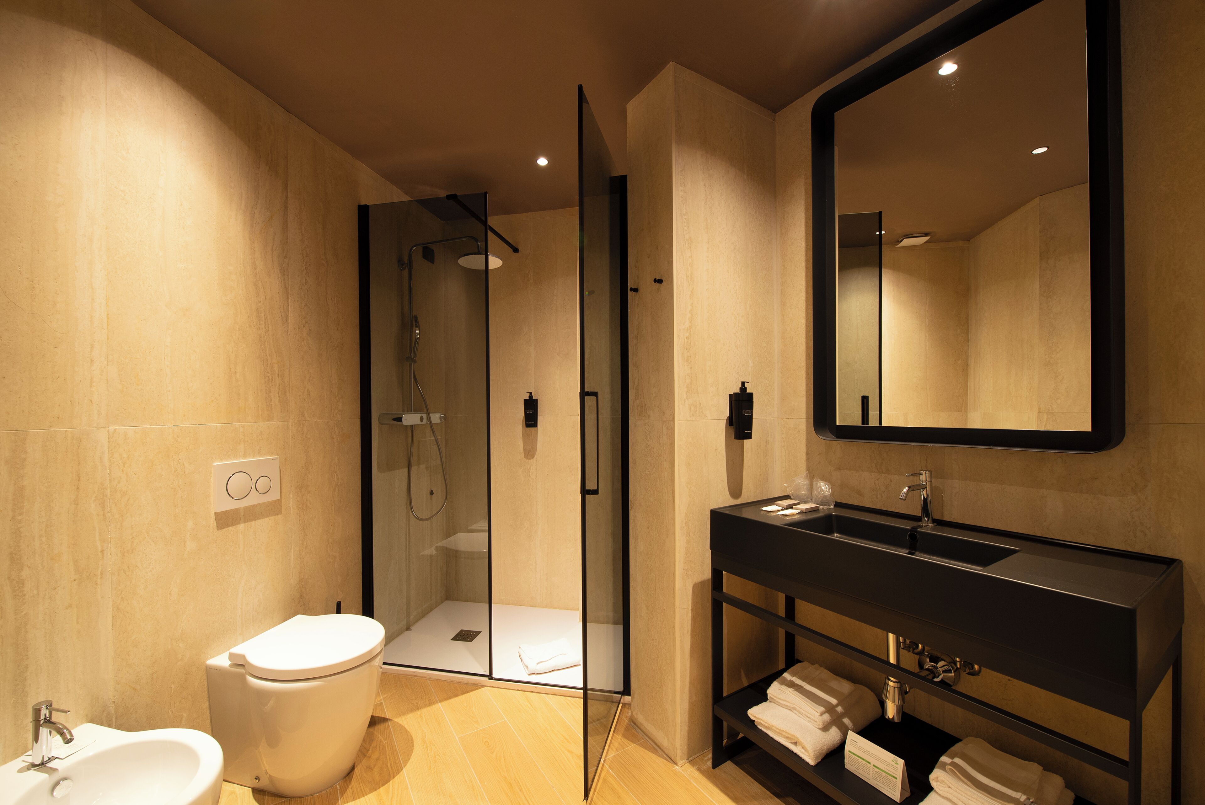 A modern bathroom with a glass-enclosed shower, a white toilet, a black sink, and a large mirror.
