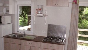Une cuisine de taille réduite, équipée d’un évier, d’une cuisinière et d’une fenêtre donnant sur un espace verdoyant.