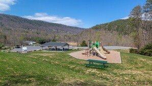 Ein Park mit Picknicktischen, einem Spielplatz und schöner Aussicht auf Hügel und einen See.