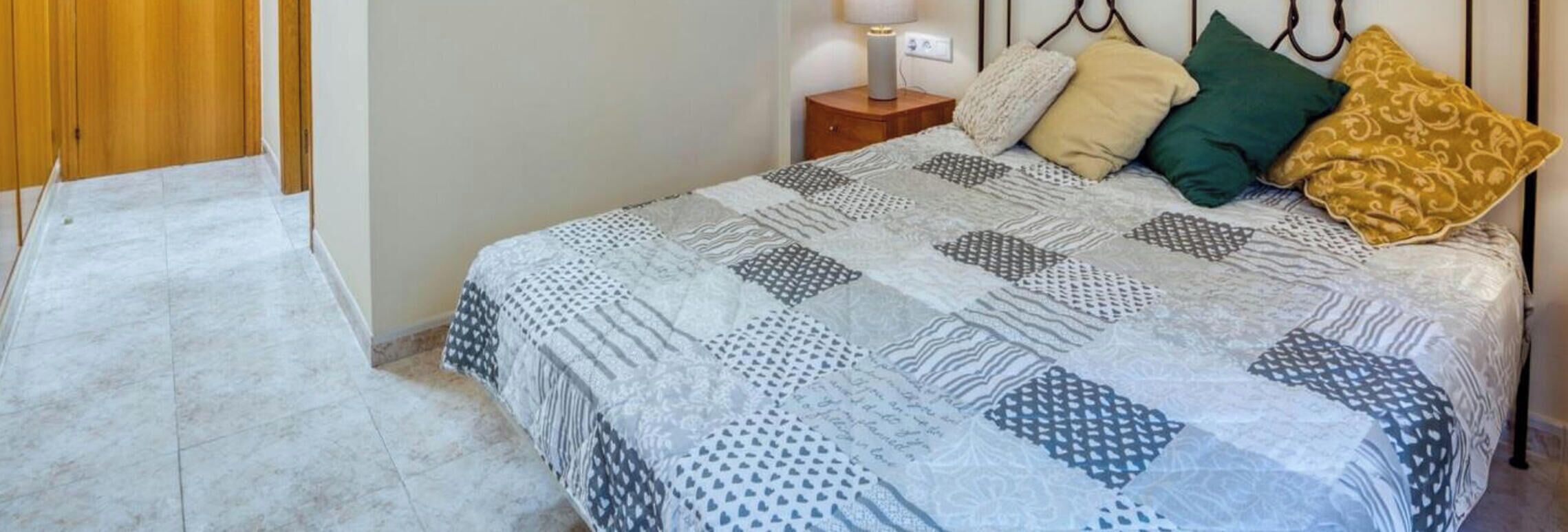 A bed with a patterned bedspread, a bedside table with a lamp, and a wooden wardrobe.