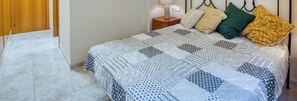 Een bed met een gebedrukte spreideken, een nachtkastje met een lamp en een houten garderobe.