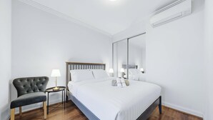 A modern hotel room with a large bed, a side table with a lamp, a dark upholstered chair, and a large mirror. - MetaWiseBnB 1BR Sleep 3 Perfect for Easter Show W Parking (Sydney Olympic Park)
