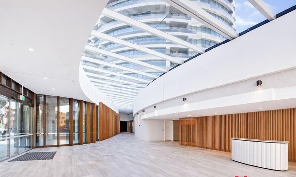 Un interior modern amb un sostre de vidre corbat, parets de panells de fusta i una zona de recepció central.