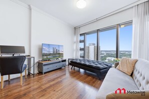 Ein modernes Wohnzimmer mit einer Couch, einem Fernseher und Blick auf die Stadt.