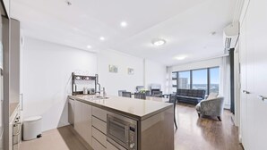 A modern kitchen with a central island, built-in oven, and a dining area with a sofa and chairs. - MetaWiseBnB 1BR Sleep 3 Perfect for Easter Show W Parking (Sydney Olympic Park)