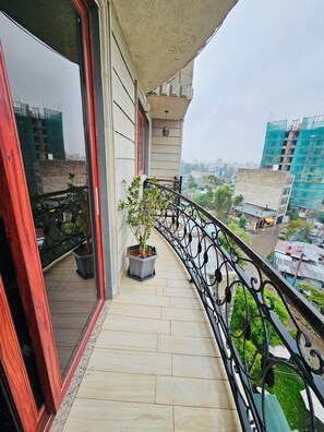 Een balkon met potplanten, uitzicht op de stadsgezicht en een gebouw met steiger.