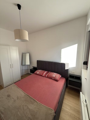 A bedroom with a bed, a wardrobe, a bedside table, a lamp, and a window.