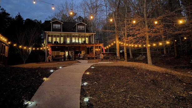 Een tweelaags huis met een overdekte veranda, lichtjes en een pad naar de ingang.