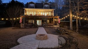 Een tweelaags huis met een overdekte veranda, buitenmeubels en lichtjes.