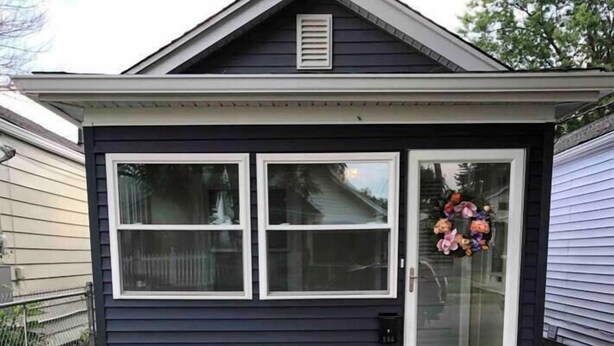 A house with a dark blue exterior, a front door with a glass panel, and a small porch area with a flower arrangement. - Louisville's Central "Lilly Pad" (Louisville)