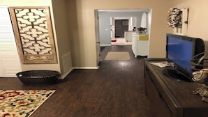 A hallway with a dark wooden floor, a basket, a decorative wall panel, and a television on a stand. - Louisville's Central "Lilly Pad" (Louisville)