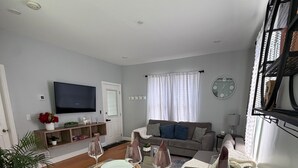 Un coin repas avec une table dressée pour quatre personnes, un canapé, un téléviseur et une fenêtre avec des rideaux.