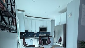 Un coin repas avec une table dressée pour quatre personnes, une cuisine en arrière-plan et un escalier sur la gauche.