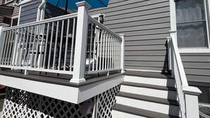 Une terrasse d’habitation avec un parasol bleu, des rampes blanches et un escalier menant à la maison.