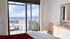 A bedroom with a large bed, a dresser, a chair, and a sliding glass door leading to a balcony with a city view. - Marinsa Beach - Penthouse (Torrox)