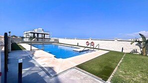 Una piscina con vistas claras al mar, un flotador salvavidas y un edificio moderno al fondo.