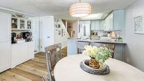 Une cuisine moderne avec des meubles blancs, une table à manger avec des chaises et un luminaire suspendu.
