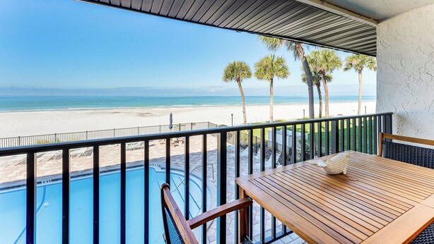 Un balcon avec vue sur la plage, une piscine et une table en bois.