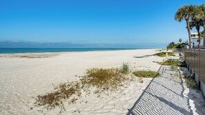Une plage avec un ciel dégagé, un rivage sablonneux et un bâtiment doté d’un balcon donnant sur la plage.