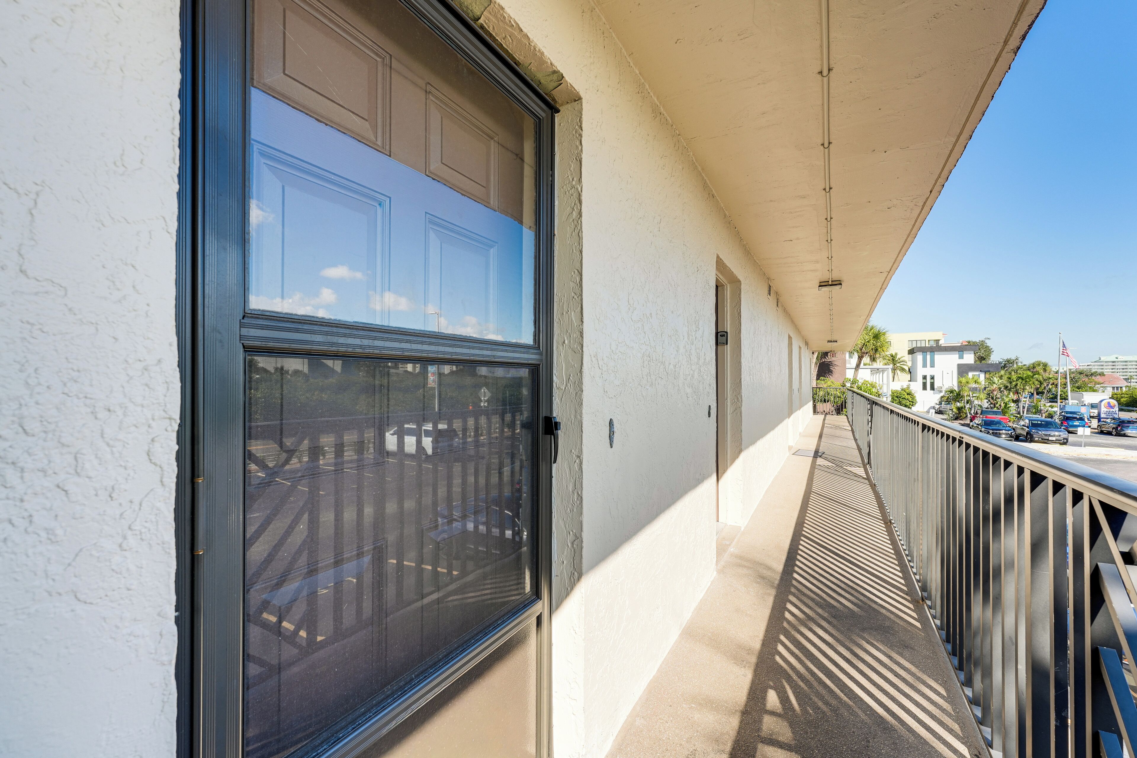 A balcony with a metal railing, a white wall, and a clear sky.