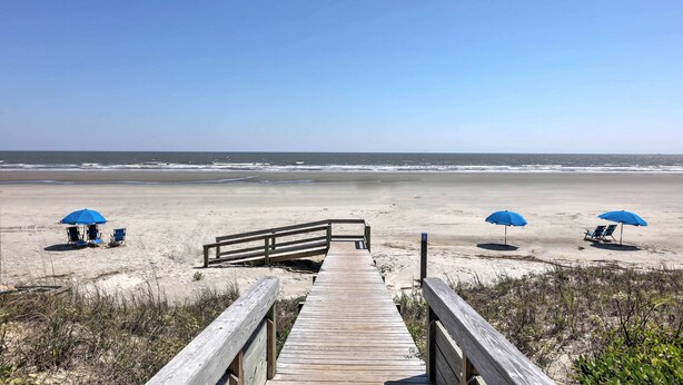 A wooden boardwalk leading to a beach with two blue umbrellas and beach chairs. - Enjoy Coastal Living! Condo on Kiawah Island (Kiawah Island)