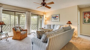 A room with a ceiling fan, a wicker chair, a striped sofa, and a window with curtains. - Enjoy Coastal Living! Condo on Kiawah Island (Kiawah Island)