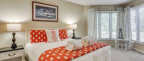 A neatly made bed with a red and white patterned bedspread, two bedside lamps, a framed picture on the wall, and a window with curtains.