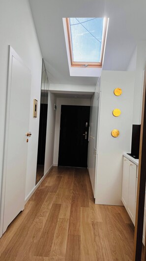 A hallway with a skylight, wooden flooring, white walls, and a black door at the end. - The Perfect Cozy Oasis (Kraków)