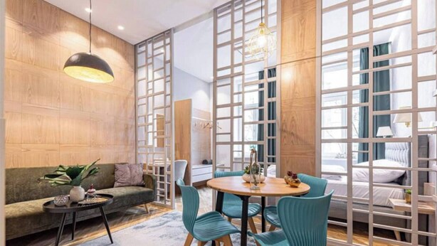 A modern hotel room with a wooden wall, a round dining table with chairs, a sofa, and a bed with a view. - The Perfect Cozy Oasis (Kraków)