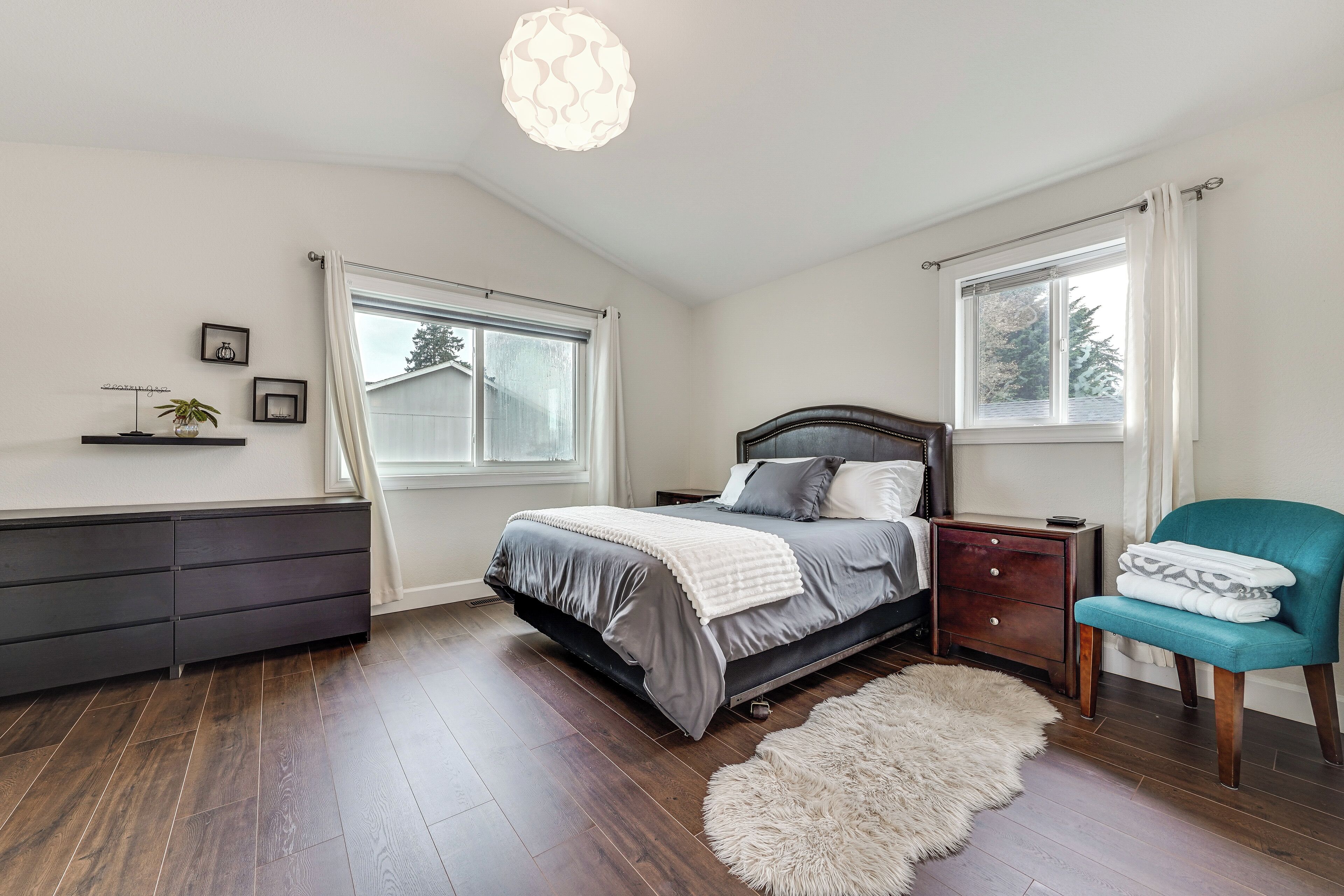 A bedroom with a bed, dresser, chair, and windows.