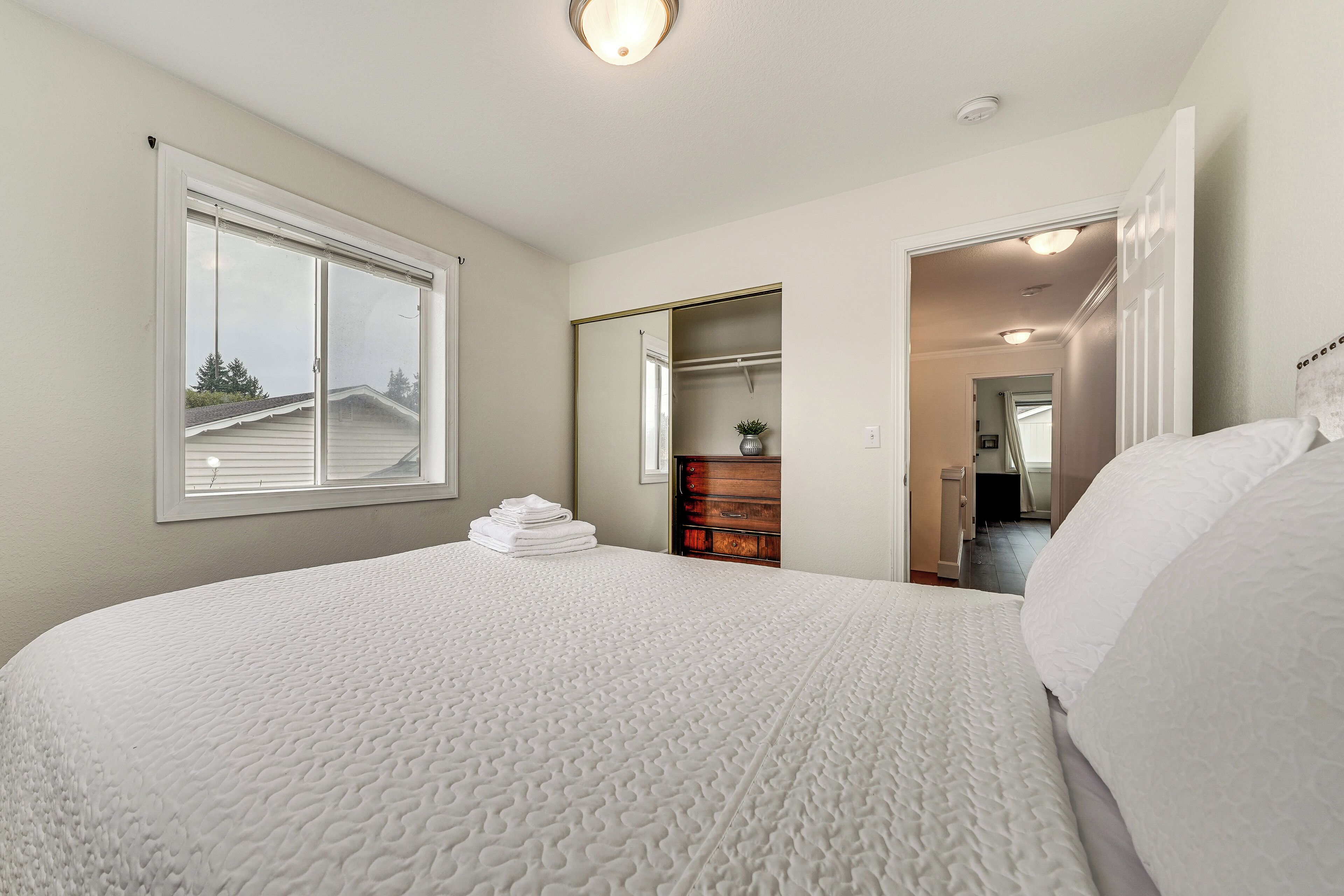 A bedroom with a large bed, a dresser, a mirror, and a window.
