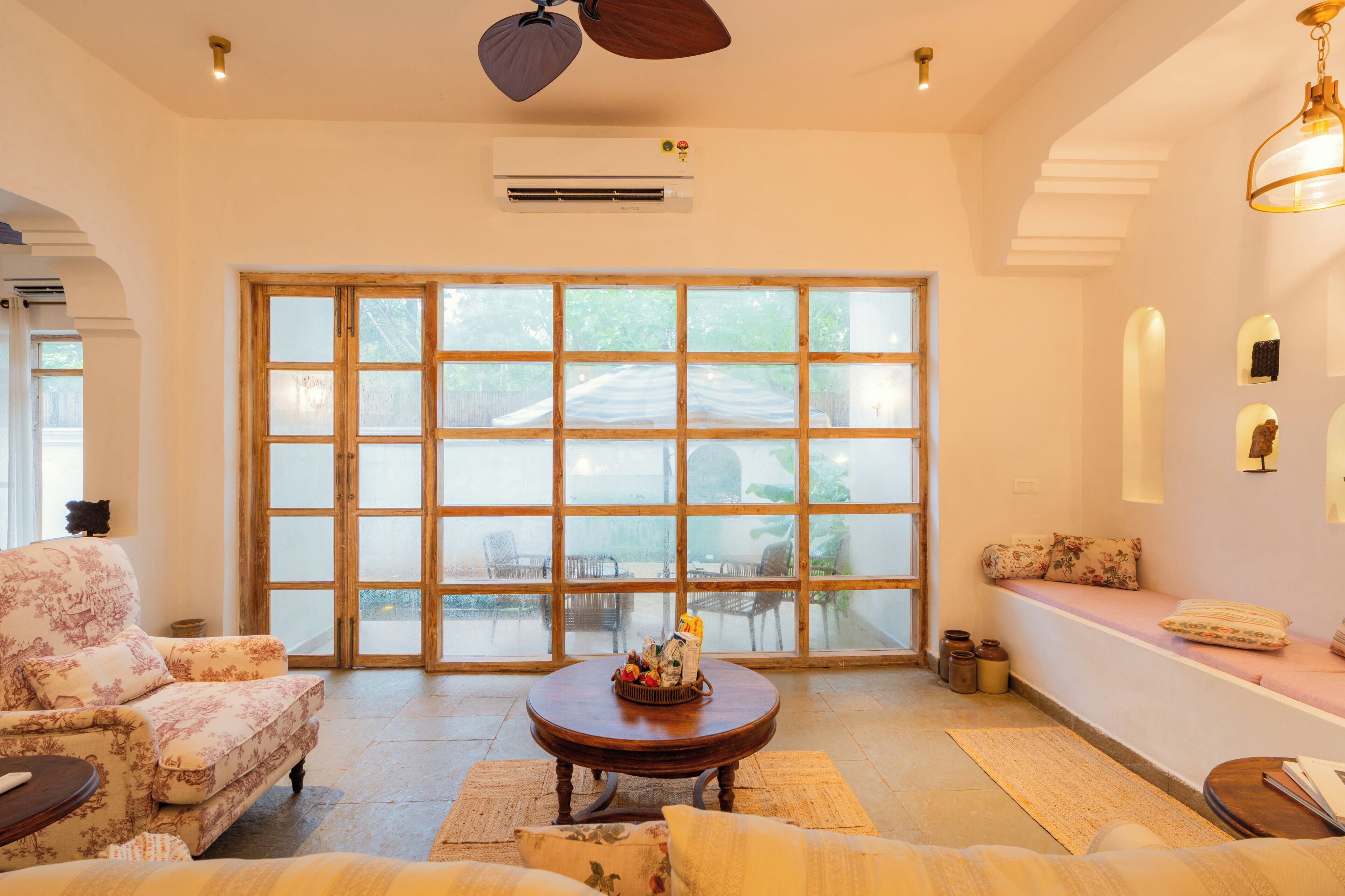 A spacious living area with a large sliding glass door, a round wooden coffee table, a sofa, and a bench with cushions.