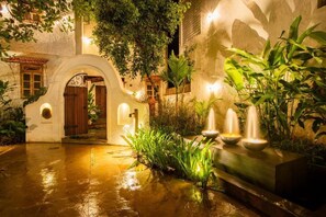 Ein Innenhof mit Brunnen, Pflanzen und einem Gebäudeeingang.