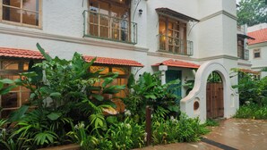 A white building with a red-tiled roof, large windows, and a lush garden with tropical plants. - ELIVAAS Amayah Rasa 4 BHK Villa (Assagao)