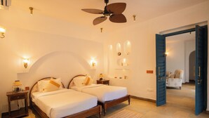 A bedroom with two beds, a ceiling fan, wall sconces, a nightstand, and a door leading to another room. - ELIVAAS Amayah Rasa 4 BHK Villa (Assagao)